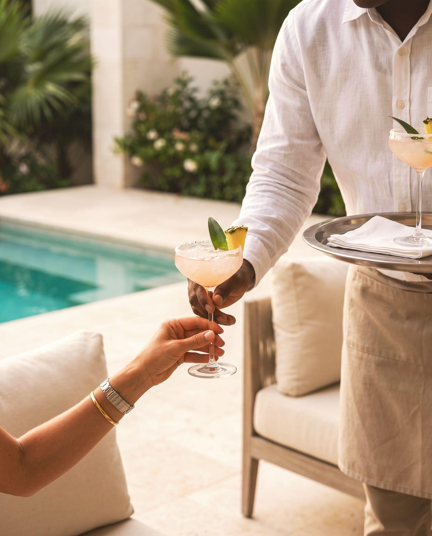 A member of villa staff serving a drink poolside