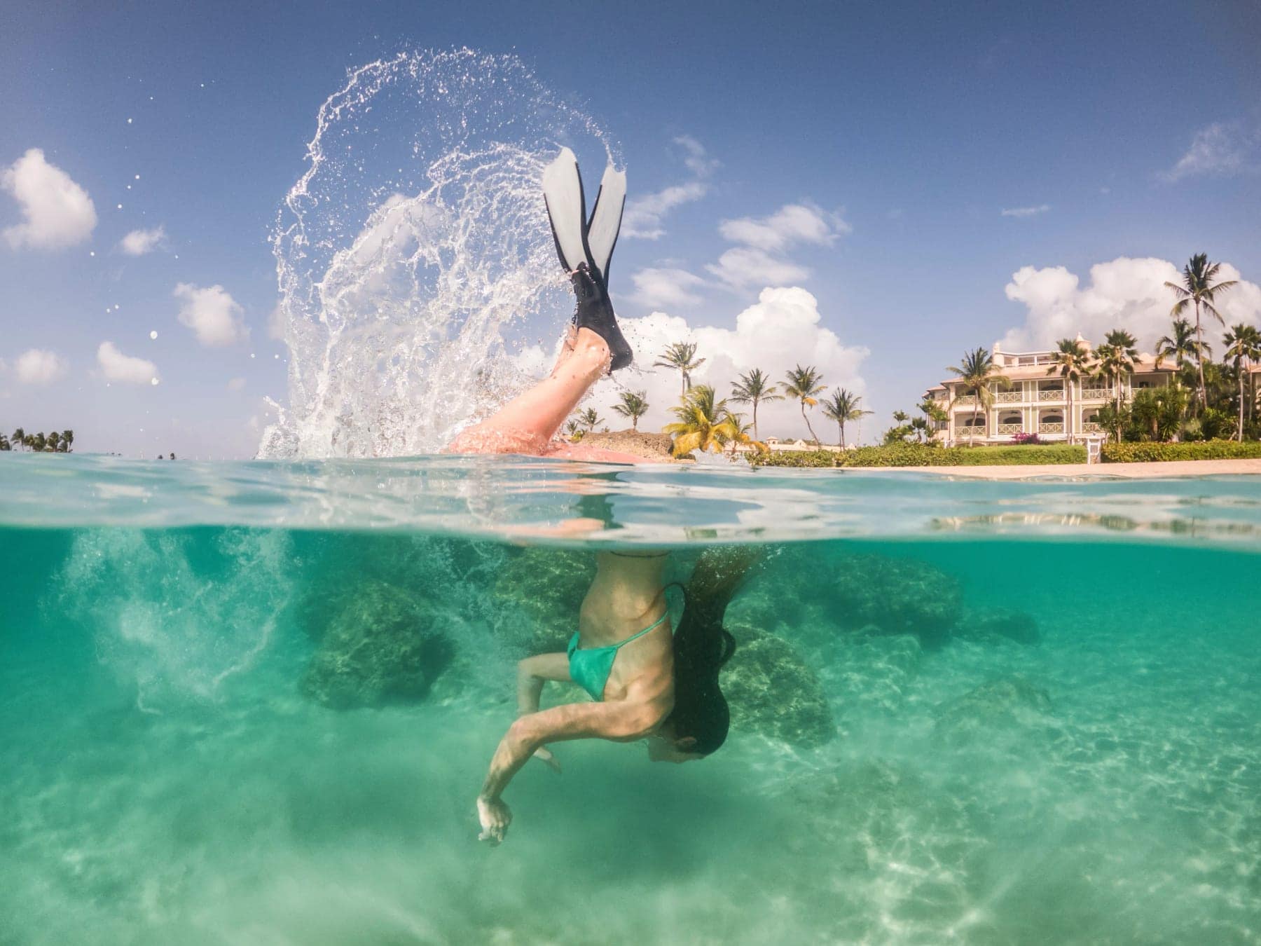 A swimmer diving into clear water off a beach lined with villas